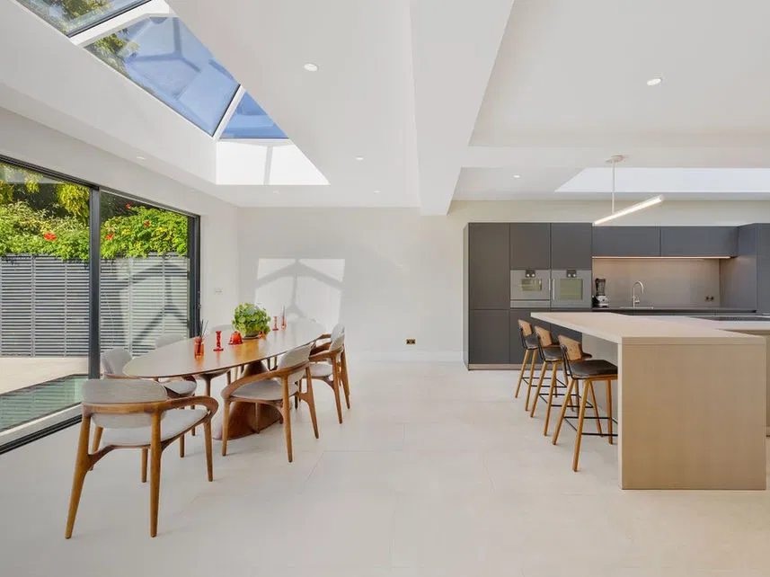 Contemporary open-plan kitchen and dining area featuring large skylights for optimal natural light, demonstrating the aesthetic of modern, sustainable builds