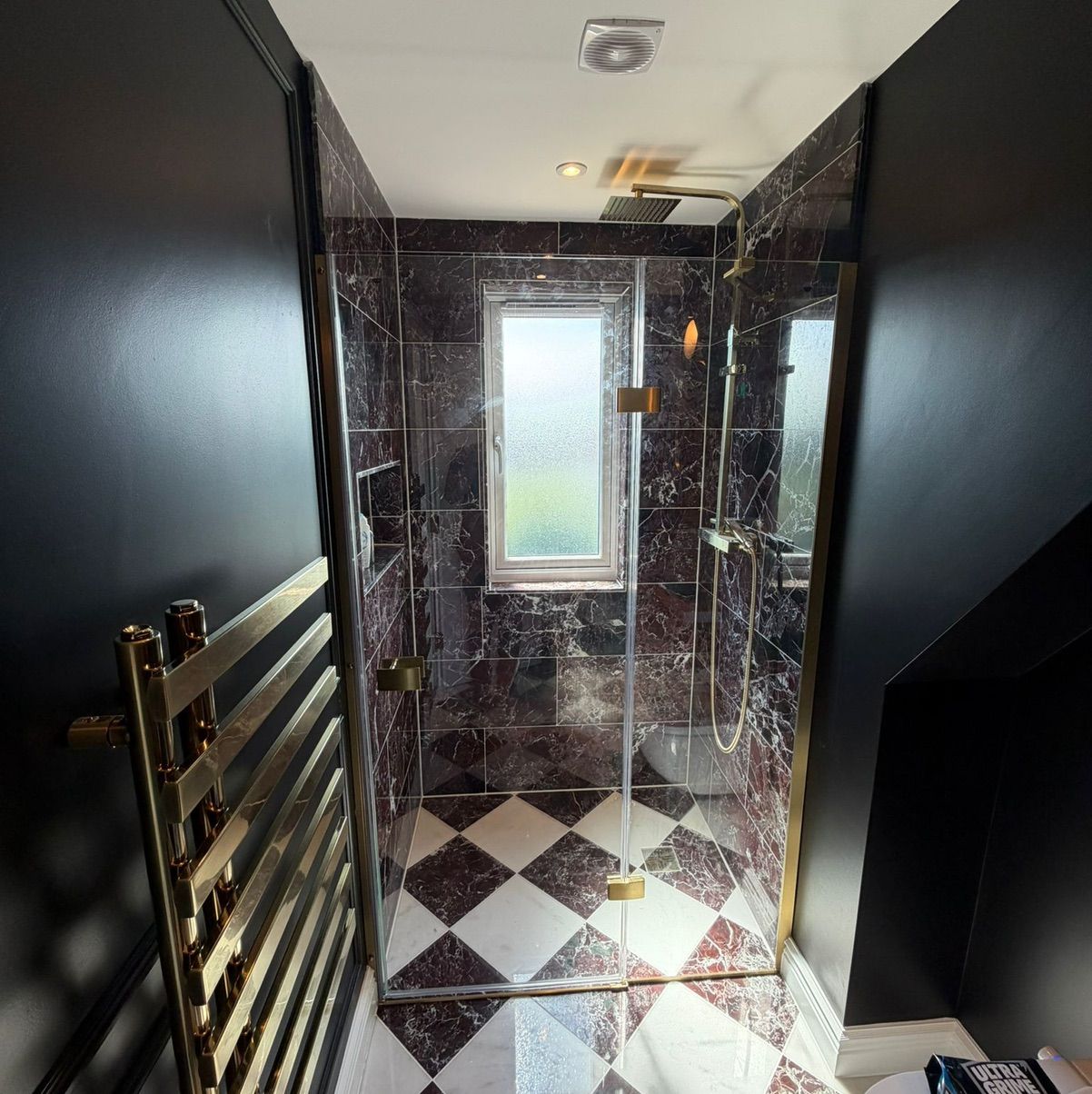 A luxury bathroom finish in a Kingston loft conversion featuring gold hardware and dark marble tiling.
